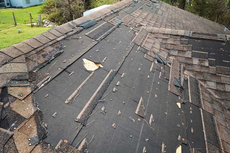 Homeowner examining loose shingles and water stains in an attic beneath a residential roof.